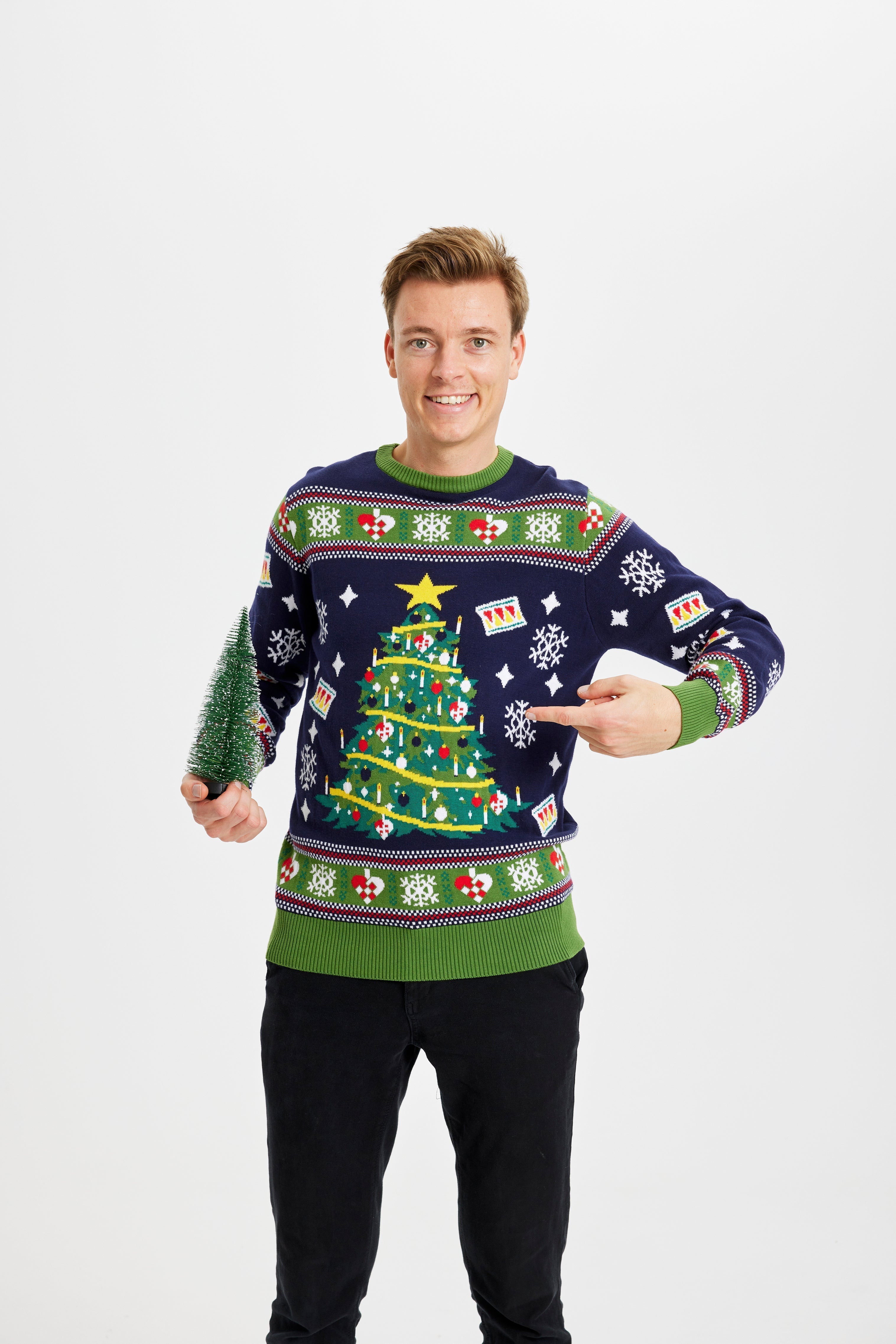 Un homme posant avec un sapin de Noël portant un pull bleu et vert avec un sapin de Noël.